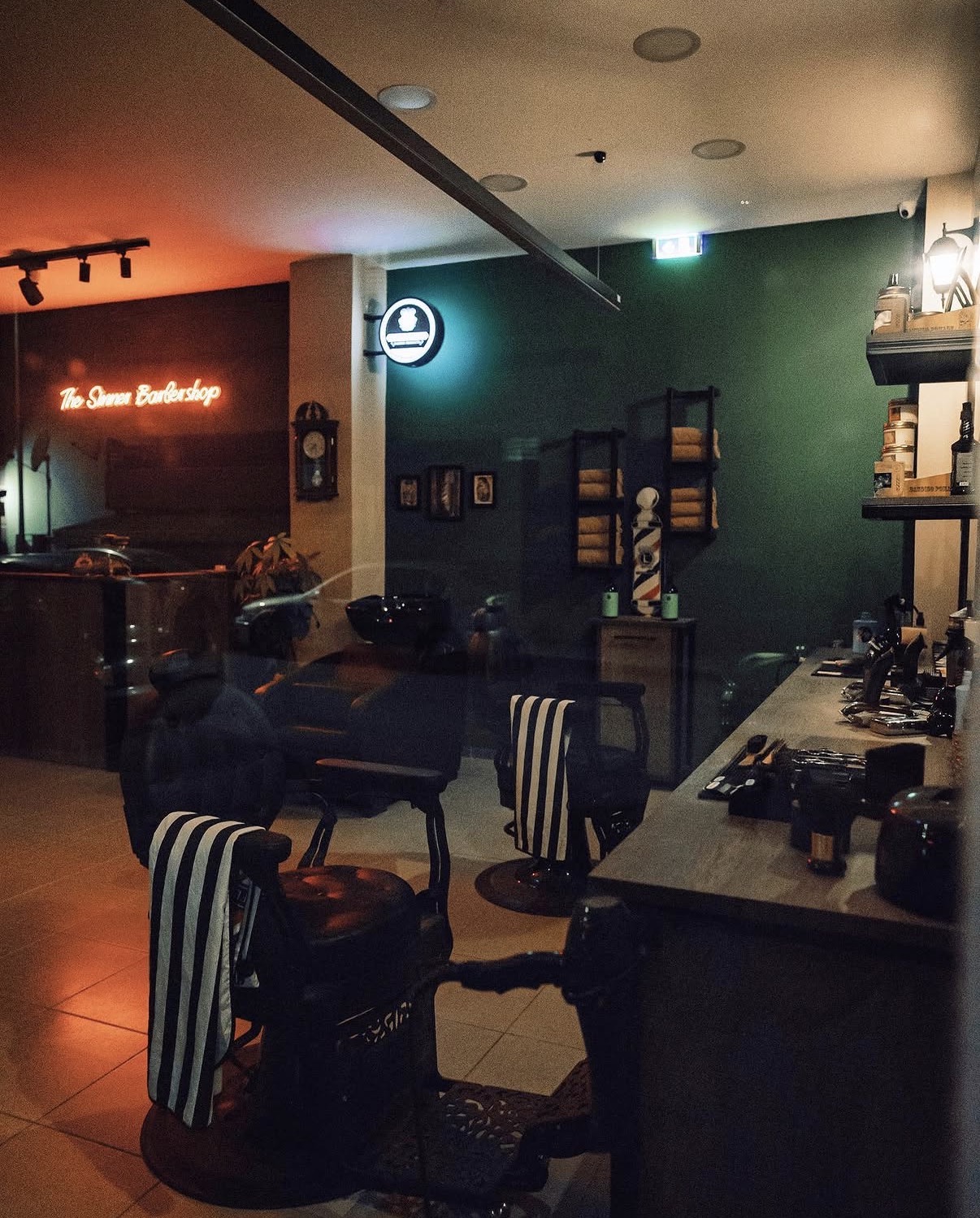 Το εσωτερικό του The Sinner Barbershop με σμαραγδί τοίχους και κόκκινο neon